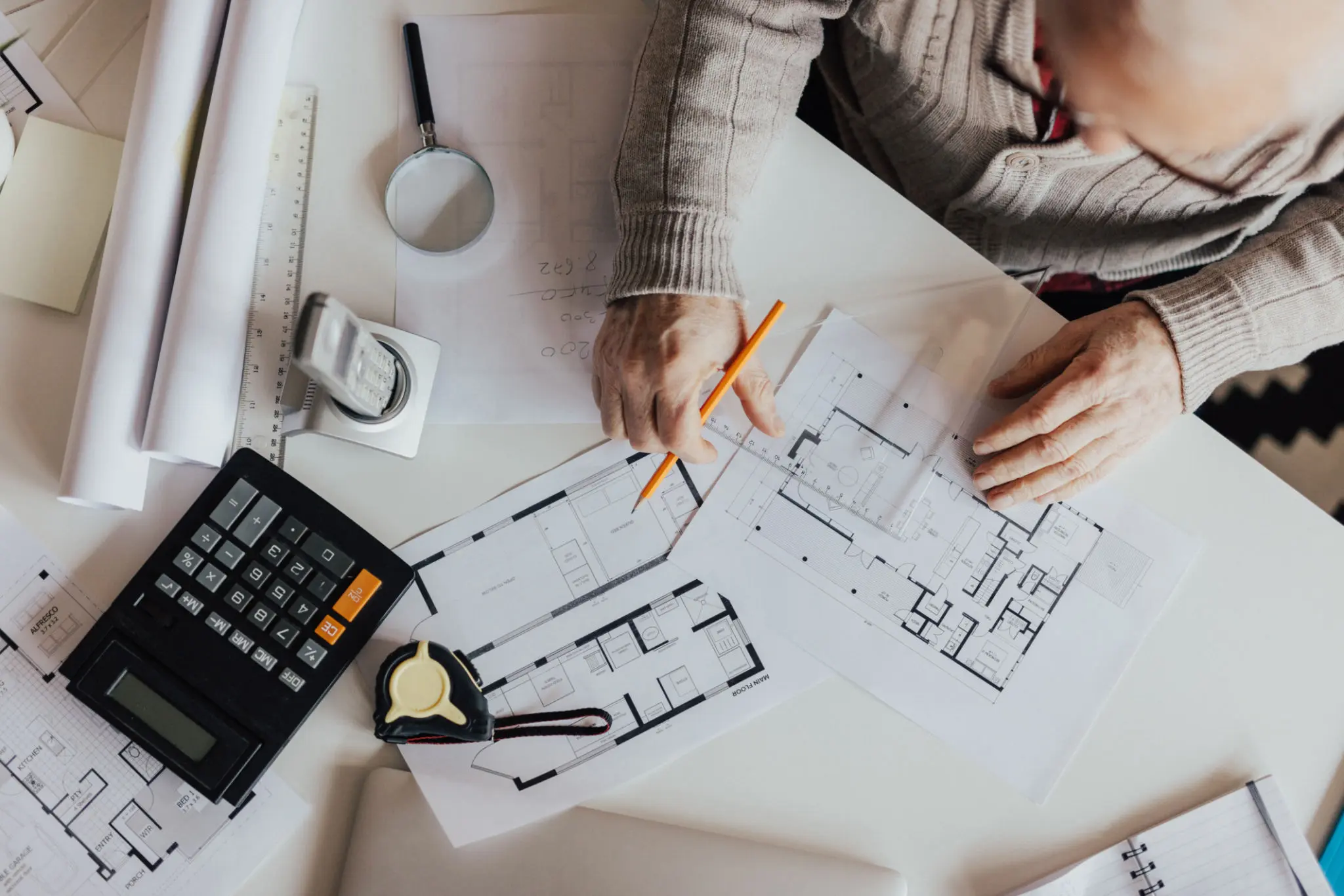 Architect reviewing blueprints with calculator and tools.