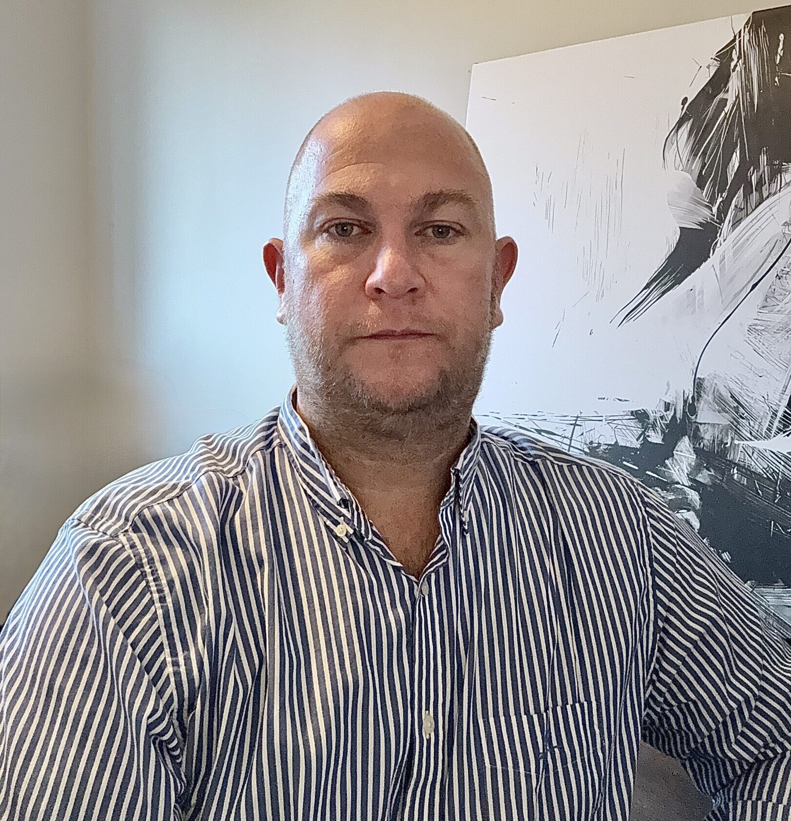 Man in striped shirt posing indoors with artwork behind him.
